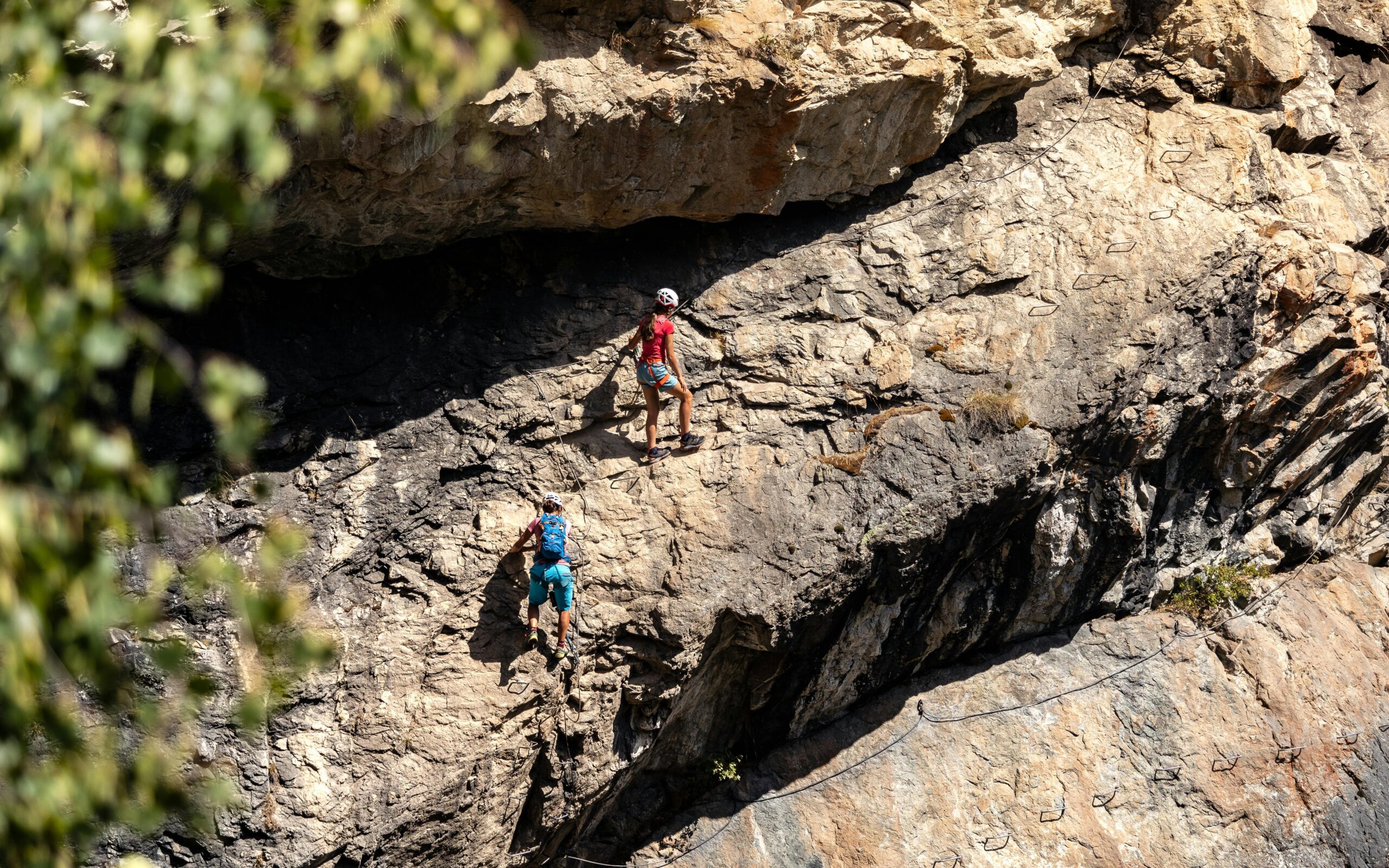 A climber struggling under heavy gear on a rock wall